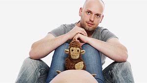 Partner sitzt über dem Babybauch mit Kuscheltier