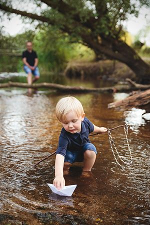 Kind spielt mit Papierboot im Bach