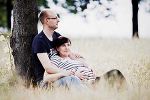 Pärchen mit Babybauch sitzt an einem Baum